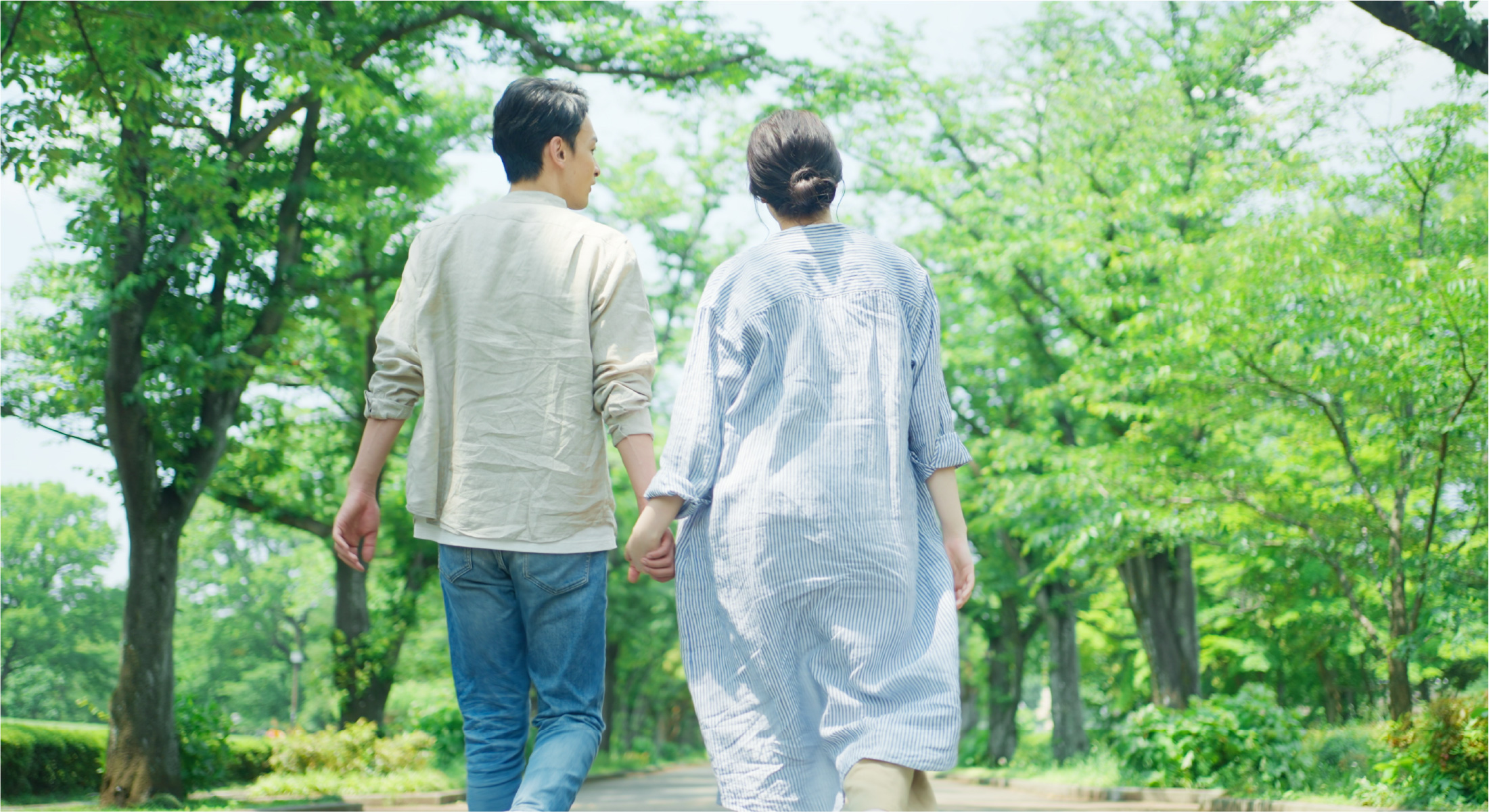 緑に囲まれた道で手をつなぐ二人